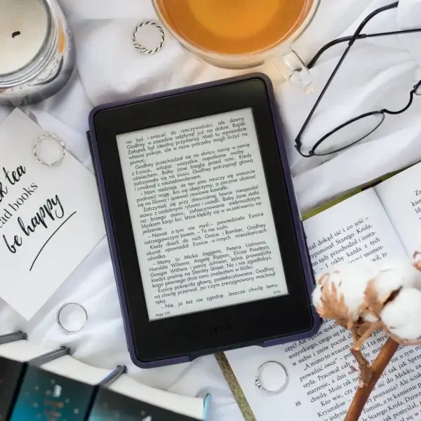 A cozy flat lay of an ebook reader with a cup of tea, open books, cotton flowers, rings, and glasses on a white background — perfect for book lovers and digital reading.